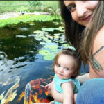 Woman and baby in front of backyard pond with koi and goldfish