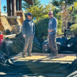Two pond contractors discussing repair strategies on a residential pond installation site. Caption: Expert pond contractors assess and strategize on maintaining the pristine condition of a backyard pond.